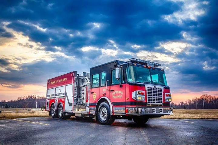 A red fire engine parked in a parkinglot with storm clouds moving in.