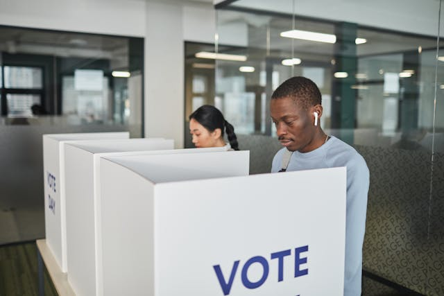 A man and a women standing inside a building voting at voting booths in an election.