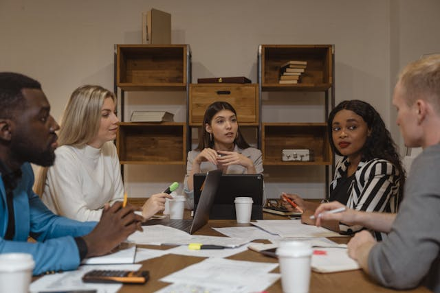 Three women and two men sitting around a table discussing an issue during a meeting.
