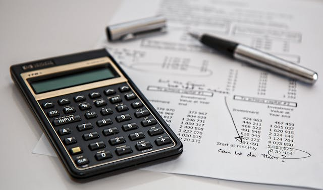 A calculator, pen, and paper resting on a table.